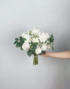 a bouquet of white flowers being held by a person's hand on a gray background