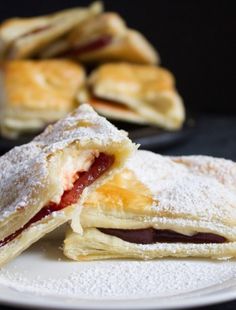 two pastries on a white plate with powdered sugar and jelly in the middle