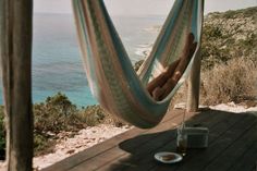 a person laying in a hammock on a wooden deck overlooking the ocean and beach