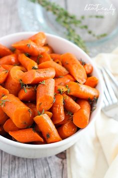 a white bowl filled with sliced carrots on top of a wooden table next to a fork