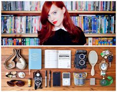 a woman with long red hair surrounded by various items on a table and in front of a bookshelf