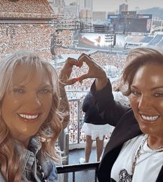 two women standing next to each other in front of a stadium full of people with their hands up