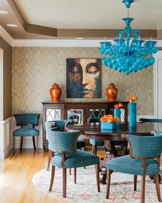 a dining room table with blue chairs and vases on top of it, in front of a painting