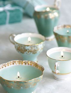 tea cups and saucers with candles in them on a white tableclothed surface