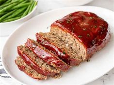 sliced meatloaf with ketchup on a white plate next to green beans