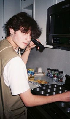 a young man is cooking in the kitchen while talking on his cell phone and looking at the camera