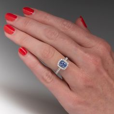 a woman's hand with red nail polish holding a blue and white diamond ring