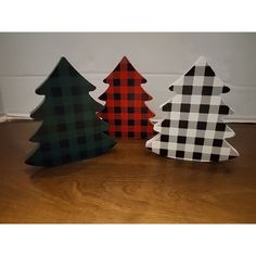 three wooden christmas trees sitting on top of a wooden floor next to a wall with a black and white checkerboard pattern