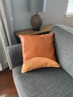 a brown pillow sitting on top of a gray couch next to a lamp and window