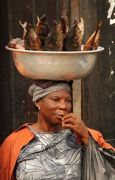 a woman with a large bowl on her head and fish in it's mouth