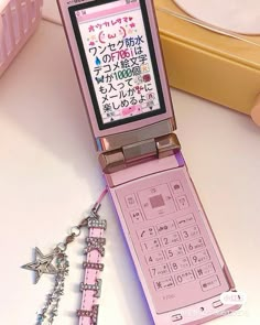 a pink cell phone sitting on top of a table next to a star charm necklace