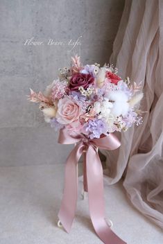 a bridal bouquet with pink and purple flowers on it, tied in a satin ribbon