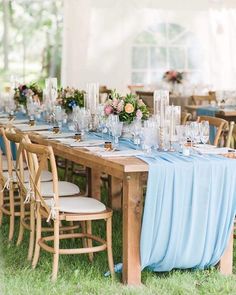 a table set up with blue linens and clear glassware for an outdoor wedding reception