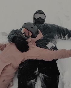 two people laying in the snow with their arms around each other