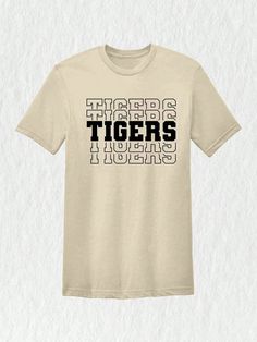 Introducing our Tigers Mascot Shirt, the perfect apparel for all the Tiger fans out there!  Whether you're a proud member of the Tigers team, a dedicated fan, or simply want to show your support, this shirt is a must-have addition to your collection. Designed with the iconic Tigers Mascot, this shirt captures the spirit and energy of your beloved team. Made with high-quality materials, this Tigers School Shirt is not only comfortable but durable as well. You'll love the softness of the fabric ag College Fan Apparel T-shirt With Team Name, Graphic Print Crew Neck T-shirt For Fans, Tri-blend T-shirt With Graphic Print For Fans, Team Spirit T-shirt With Screen Print For Fan Gear, Pre-shrunk Team-colored Fan Apparel T-shirt, School Spirit Short Sleeve T-shirt With Letter Print, Fan Apparel T-shirt With Letter Print, Team-colored Screen Print T-shirt For Fans, Team-colored T-shirt With Screen Print For Fans