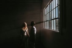 a man and woman standing next to each other in front of a window