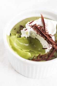 a white bowl filled with green cream and whipped cream on top of chocolate shavings