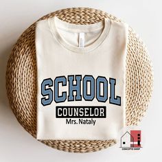 a white t - shirt with the words school counselor mrs nataly on it sitting next to a wicker basket