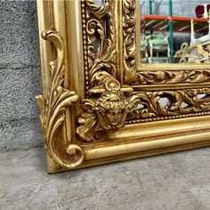 an ornate gold framed mirror sitting on the ground in front of a gray brick wall