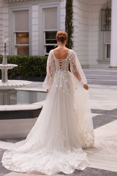 a woman in a wedding dress is standing near a fountain with her back to the camera