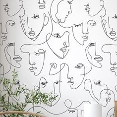 a wall with many faces on it and a plant in the corner next to it