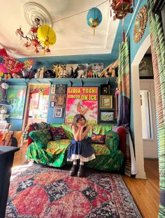 a woman sitting on top of a green couch in a room filled with pictures and decorations