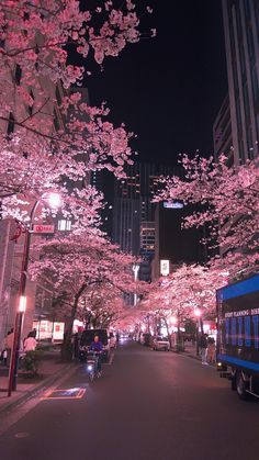 a street lined with cherry blossom trees and tall buildings in the background, at night