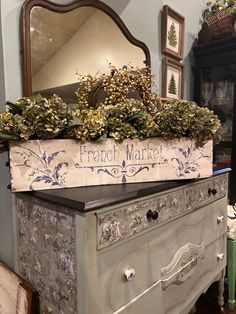 an old dresser is decorated with greenery and french market sign on it's top