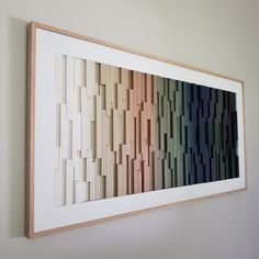 an art piece hanging on the wall in front of a white frame with multicolored squares