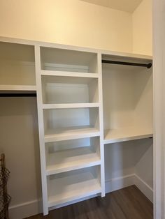 an empty walk in closet with white shelving and wood flooring on the walls