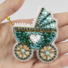 a hand holding a miniature baby carriage brooch with pearls and beads on it's side