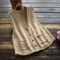 a sweater with buttons on it sitting next to a vase and some flowers in front of a wooden fence