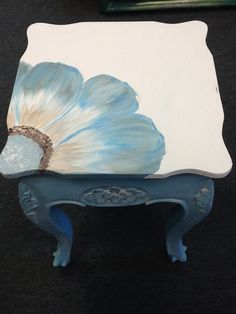 a blue and white table with a flower painted on it's side, sitting on a black surface