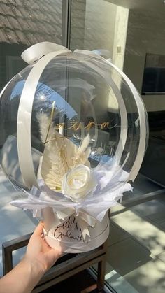 a hand holding a clear glass ball with white flowers in it and writing on the inside