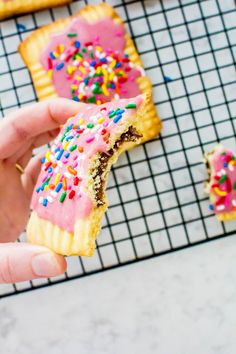 a hand holding a half eaten pastry with pink frosting and sprinkles