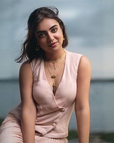 a woman sitting on top of a wooden bench next to the ocean wearing a pink dress