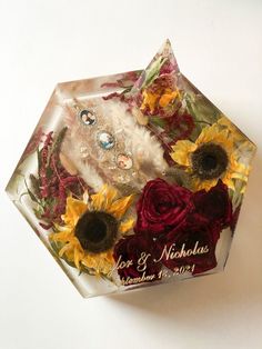 a glass box with sunflowers and other flowers in it on a white surface