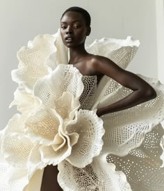 a woman in a white dress with large flowers on her shoulders and hands behind her back