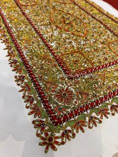 an embroidered tablecloth with red and gold trimmings on top of a white cloth