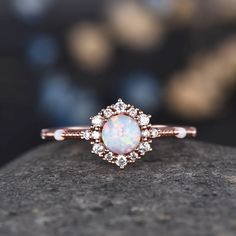 a white opal and diamond ring sitting on top of a rock