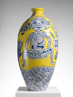 a yellow and blue vase sitting on top of a white pedestal