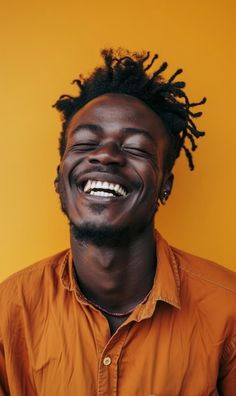 a man with dreadlocks smiling and wearing an orange shirt against a yellow background