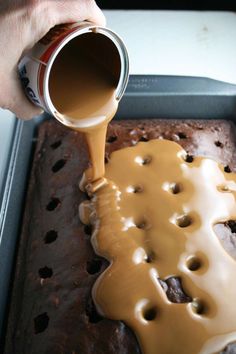 a person pouring caramel sauce on top of a chocolate cake in a baking pan