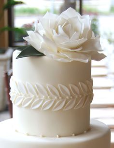 a three tiered cake with white frosting and a large flower on the top