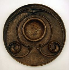 an old metal plate with swirls and scrolls on the front, against a white background