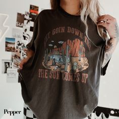 Stand out at the rodeo or country music festival with this "Ain't Going Down" shirt. Perfect for the cowgirl in your life, this Western retro tee features a unique graphic inspired by Garth Brooks' hit "Til the Sun Comes Up." Made with comfort colors, this cowboy shirt is a great gift for her and an essential addition to any country music lover's wardrobe. Get your hands on this stylish and trendy piece that combines classic Western vibes with a touch of modern flair. A must-have for those who love to embrace their country roots in style. Our team at The Southern Thistle is always happy to bring your ideas to life. If you have a custom design in mind, please send us a message or email us at info@thesouthernthistle.com to discuss your vision. With a 5-star rating, you can trust in the quali Country Music Shirt, Western Vibes, Country Music Festival, Country Music Shirts, Rodeo Shirts, Cowboy Shirt, Garth Brooks, Cowboys Shirt, Retro Tee