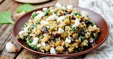 a brown bowl filled with rice and vegetables on top of a wooden table next to garlic