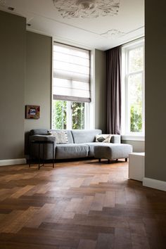 a living room with wood flooring and large windows in the corner, along with an l - shaped couch