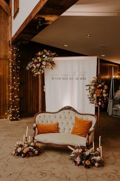 a couch and some candles in front of a white sign with flowers on it at a wedding