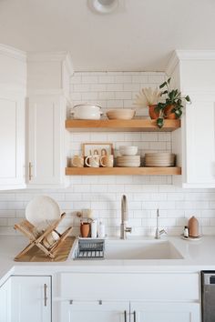 a white kitchen with open shelving above the sink and dishes on the counter top